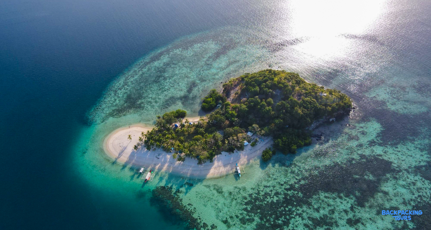 An aerial view of a pristine private island beach with clear turquoise water and boats in Coron.