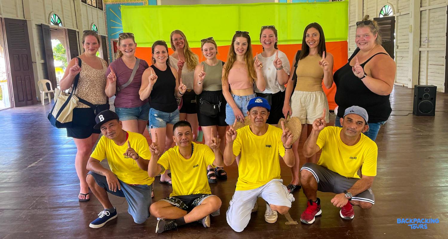 A happy group of tourists and local men pose together, holding up one finger, in Puerto Princesa.