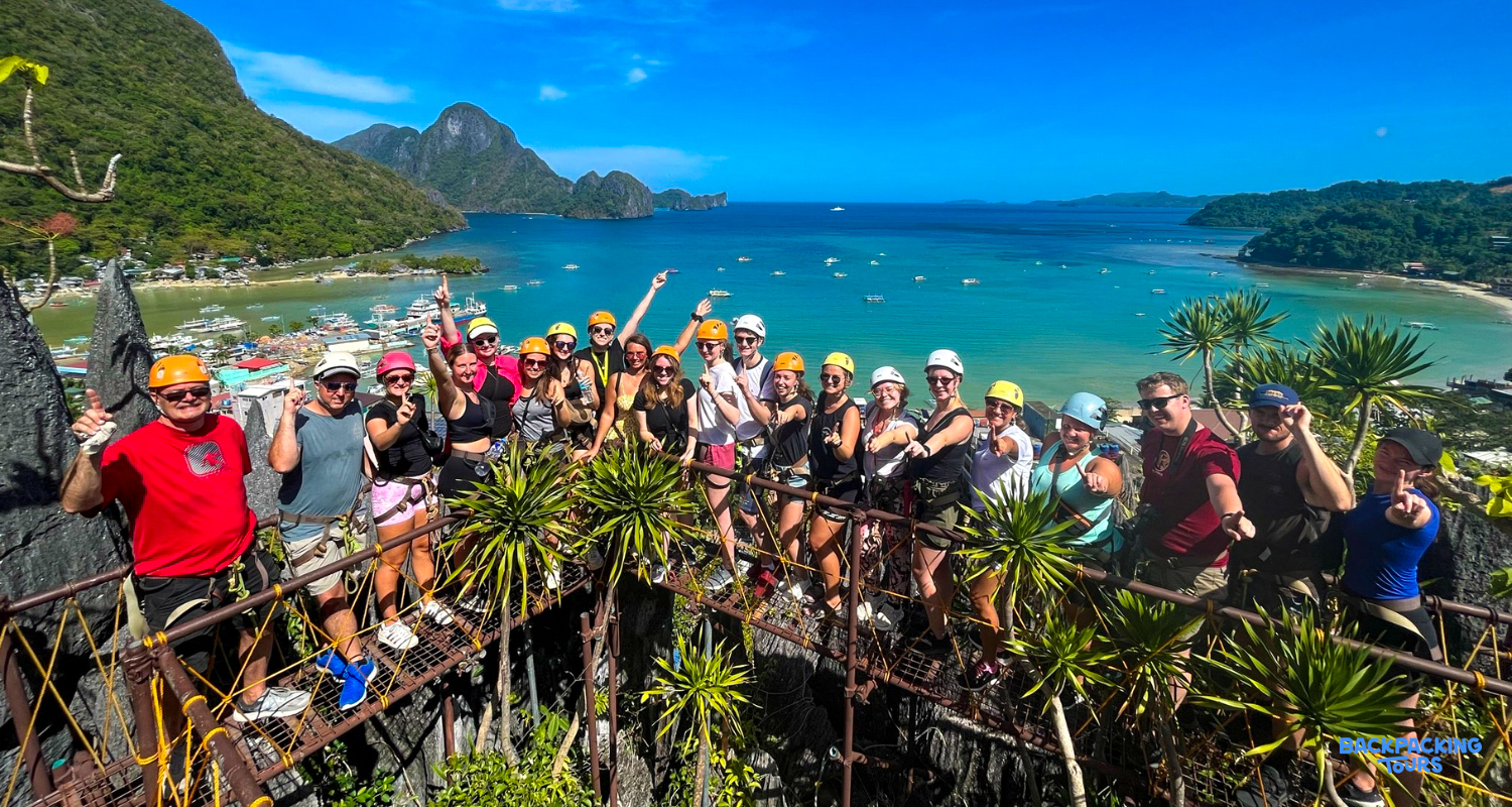 A large group of smiling backpackers on a canopy walk high above El Nido bay.