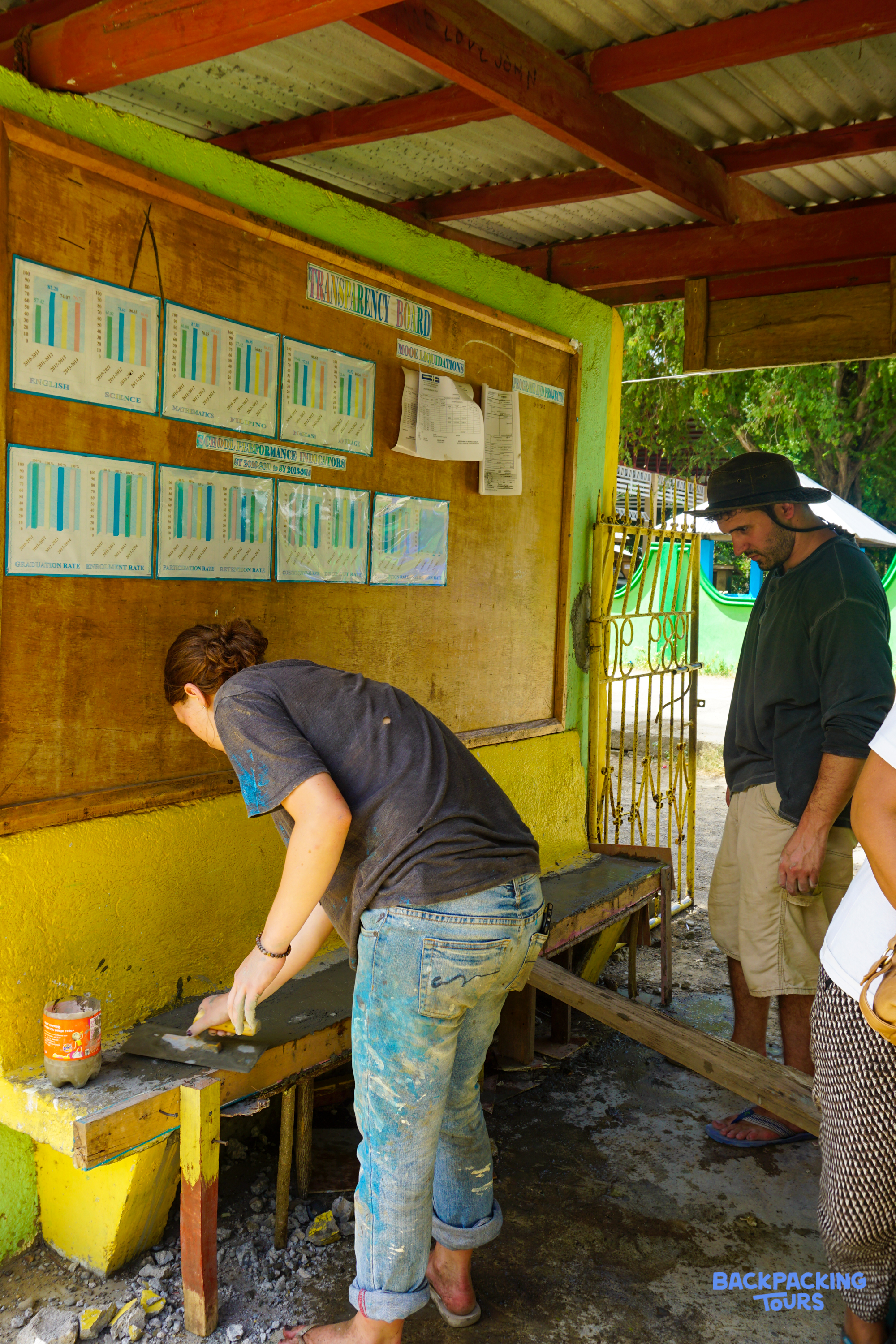 A volunteer smooths cement on a new structure while another person observes the progress.