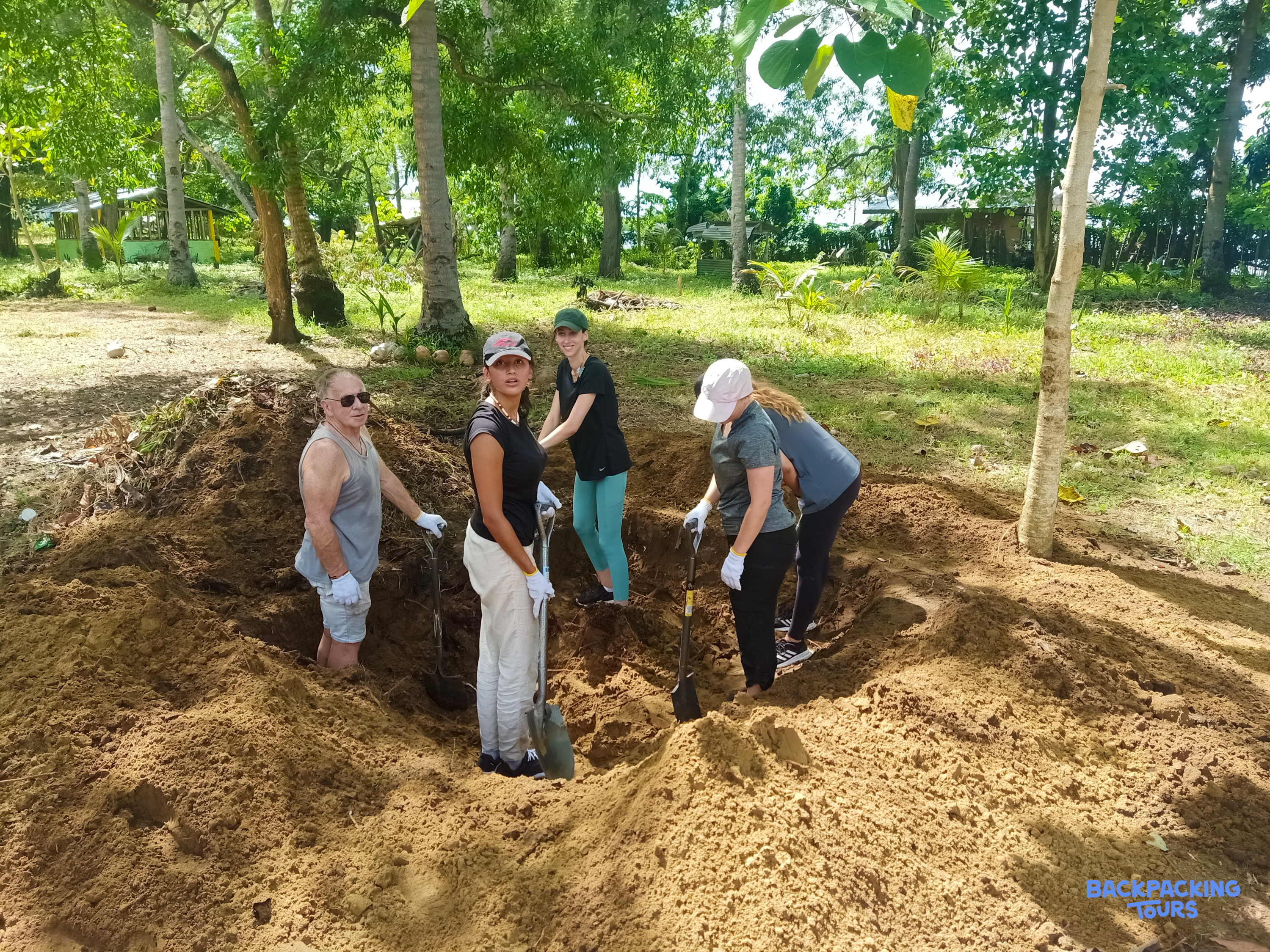 Group of volunteers actively digging a foundation pit for a new home in a tropical setting.