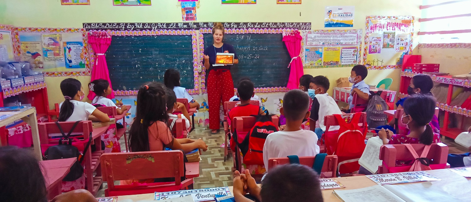 A volunteer teaches a group of young children in a colorful classroom in the Philippines.