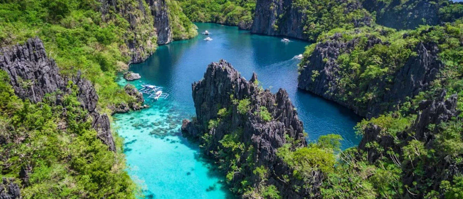 Boats navigate a breathtaking turquoise lagoon nestled among towering green-covered limestone cliffs.