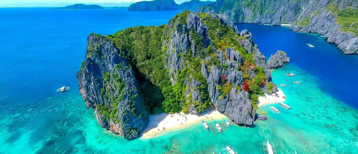 Aerial view of a stunning tropical island with limestone cliffs, white sand beach, and turquoise waters in Palawan.