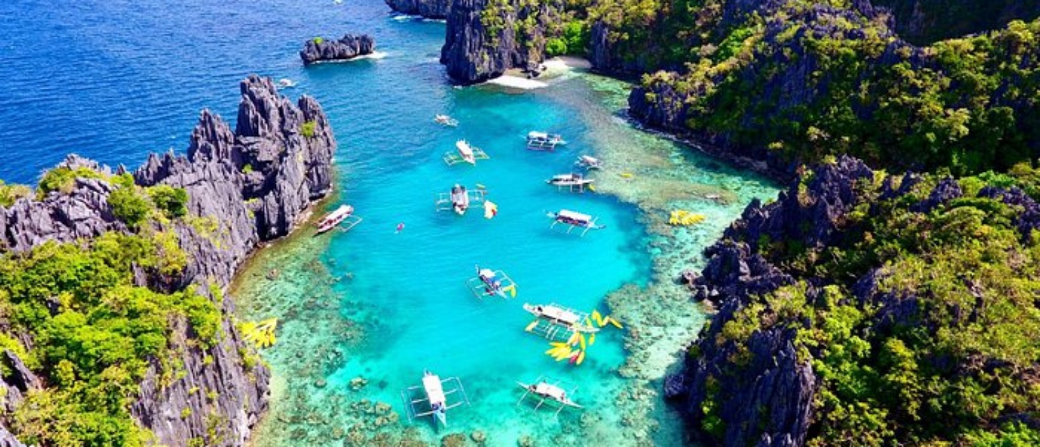 Stunning turquoise bay with traditional boats anchored among dramatic green limestone cliffs in the Philippines.