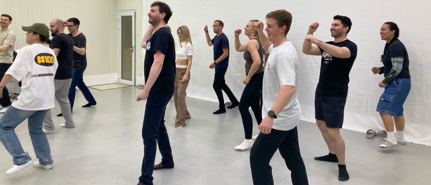 A diverse group of travellers enthusiastically learning K-pop dance moves in a bright studio in Seoul.