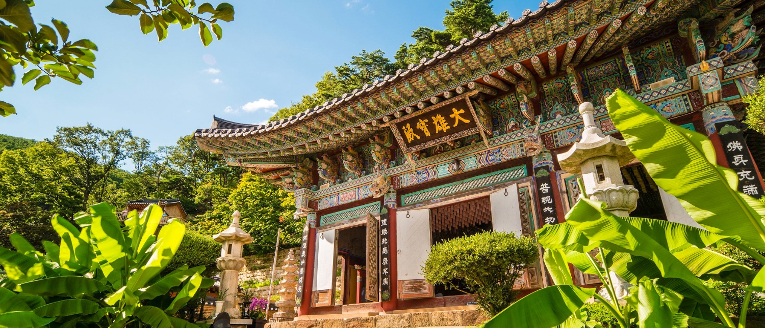 Geumsunsa Temple, a beautifully adorned traditional building, nestled among lush green trees under a blue sky.