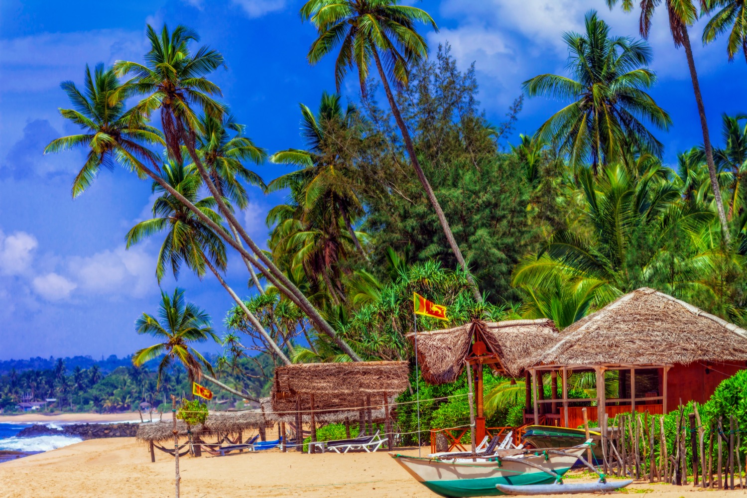 Vibrant Sri Lankan beach with golden sand, lush palm trees, charming huts, and small boats.