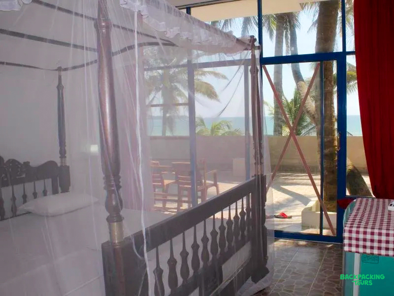 Relaxing bedroom with a four-poster bed and mosquito net, offering a beautiful ocean view in Sri Lanka.