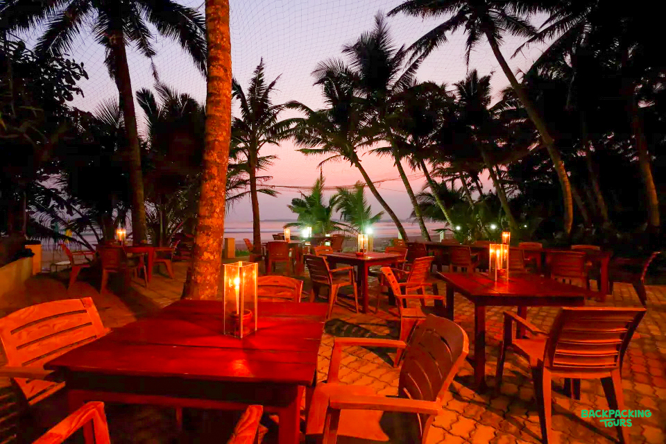 Tranquil outdoor dining setting with glowing candles and palm trees at sunset by the ocean in Mirissa.
