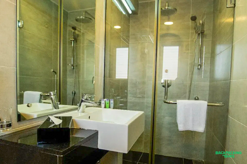A clean, modern hotel bathroom in Nuwara Eliya with a white sink, large mirror, and glass shower.