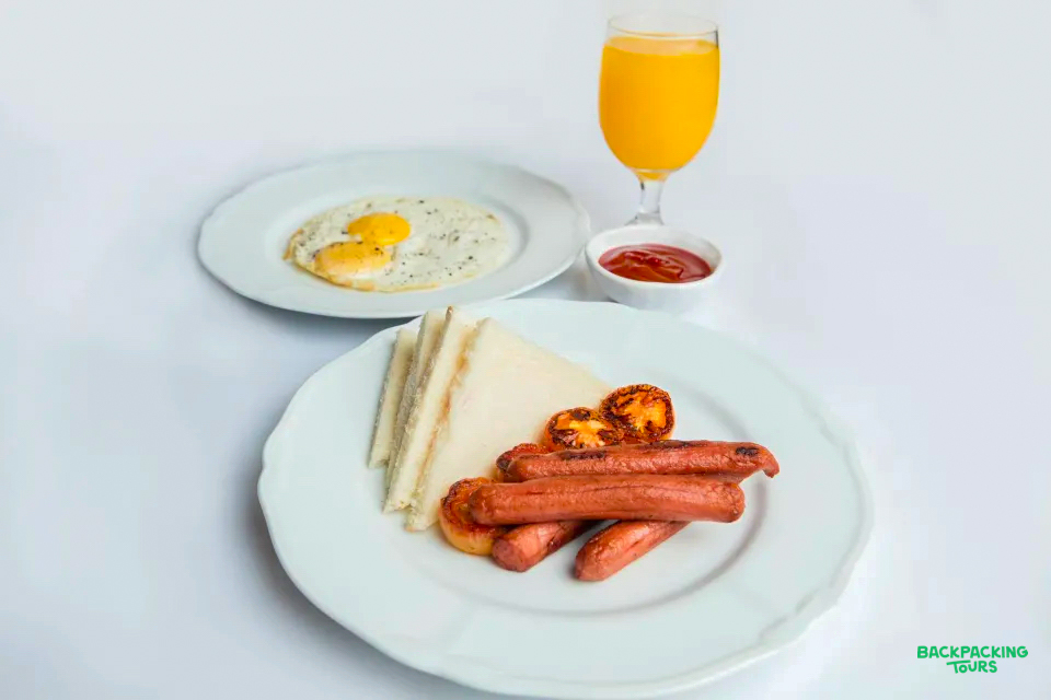 A hearty breakfast with sausages, a fried egg, grilled tomatoes, toast, and orange juice.