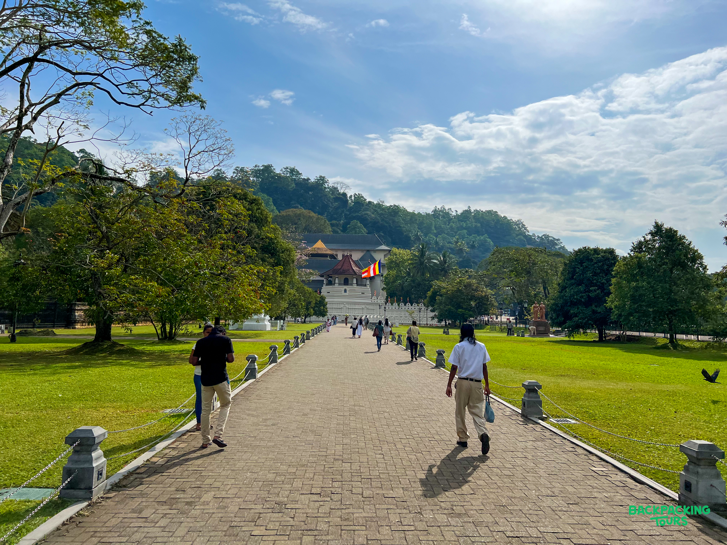 Tourists walk along a paved path towards the ornate Temple of the Tooth in Kandy, Sri Lanka.