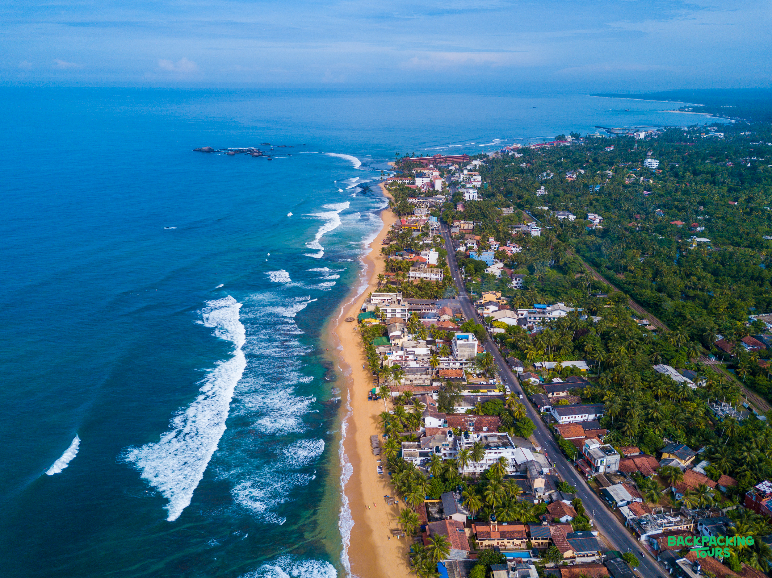 Aerial view of a vibrant coastline with sandy beaches, crashing waves, and buildings in Colombo, Sri Lanka.