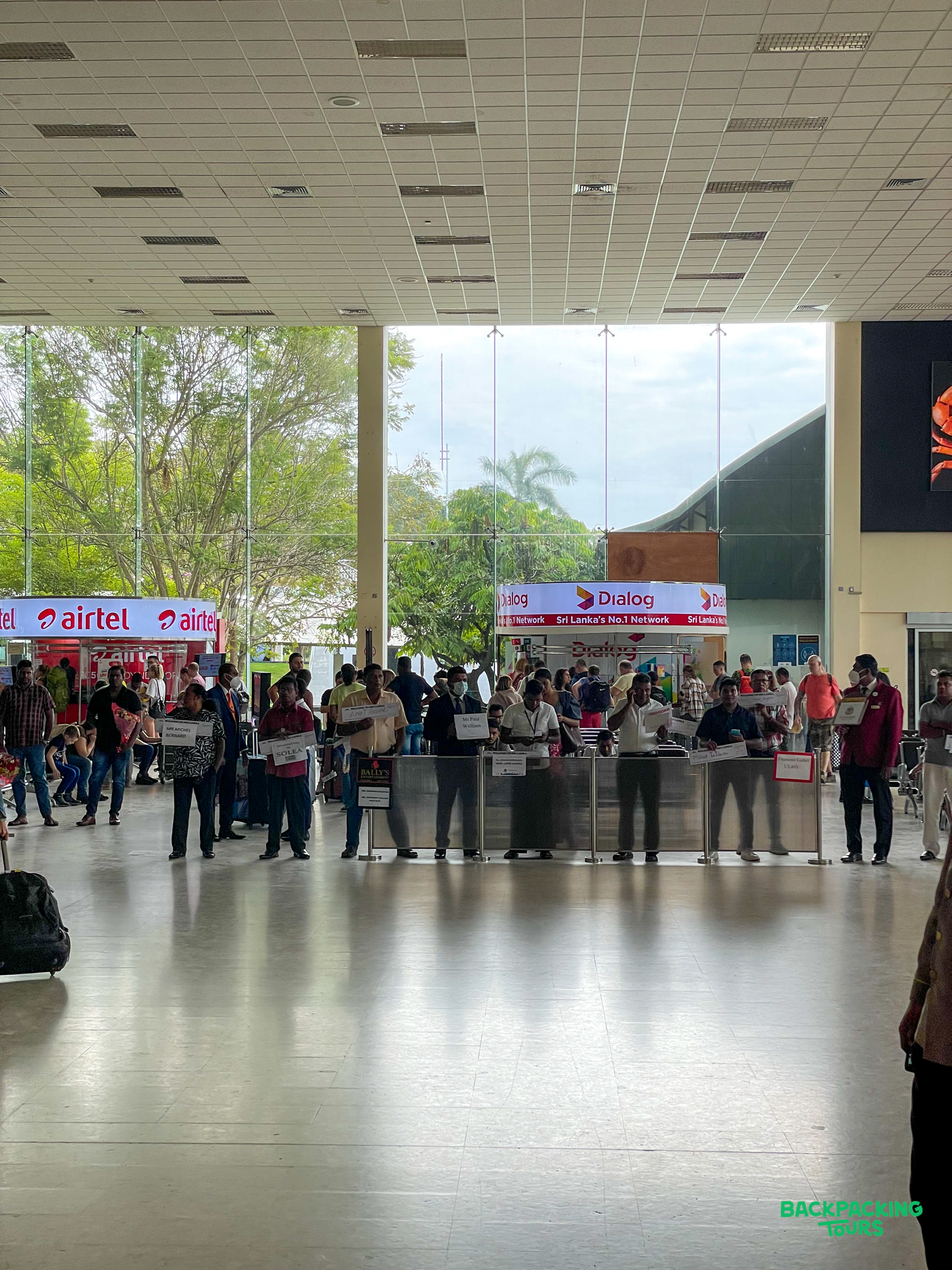 Tour representatives holding signs, waiting for arrivals in a busy Sri Lankan airport terminal.