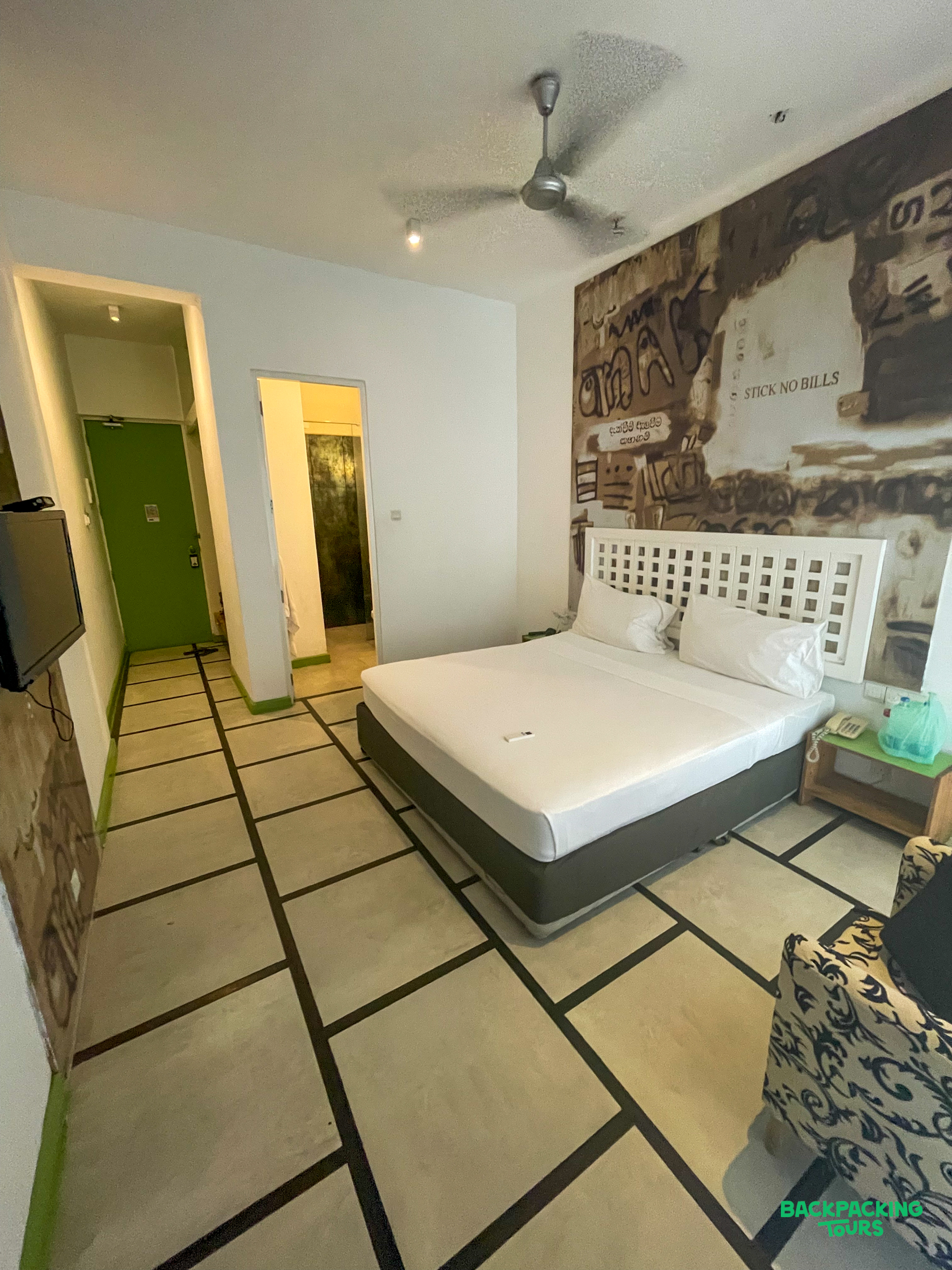 A comfortable hotel room in Colombo with a large bed, artistic wall mural, and patterned floor.