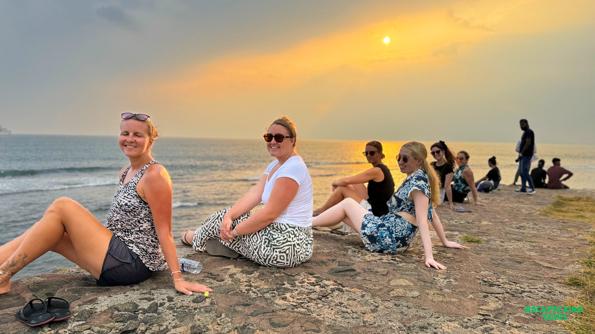 A group of friends relax on rocks by the ocean, enjoying a beautiful sunset over Weligama.