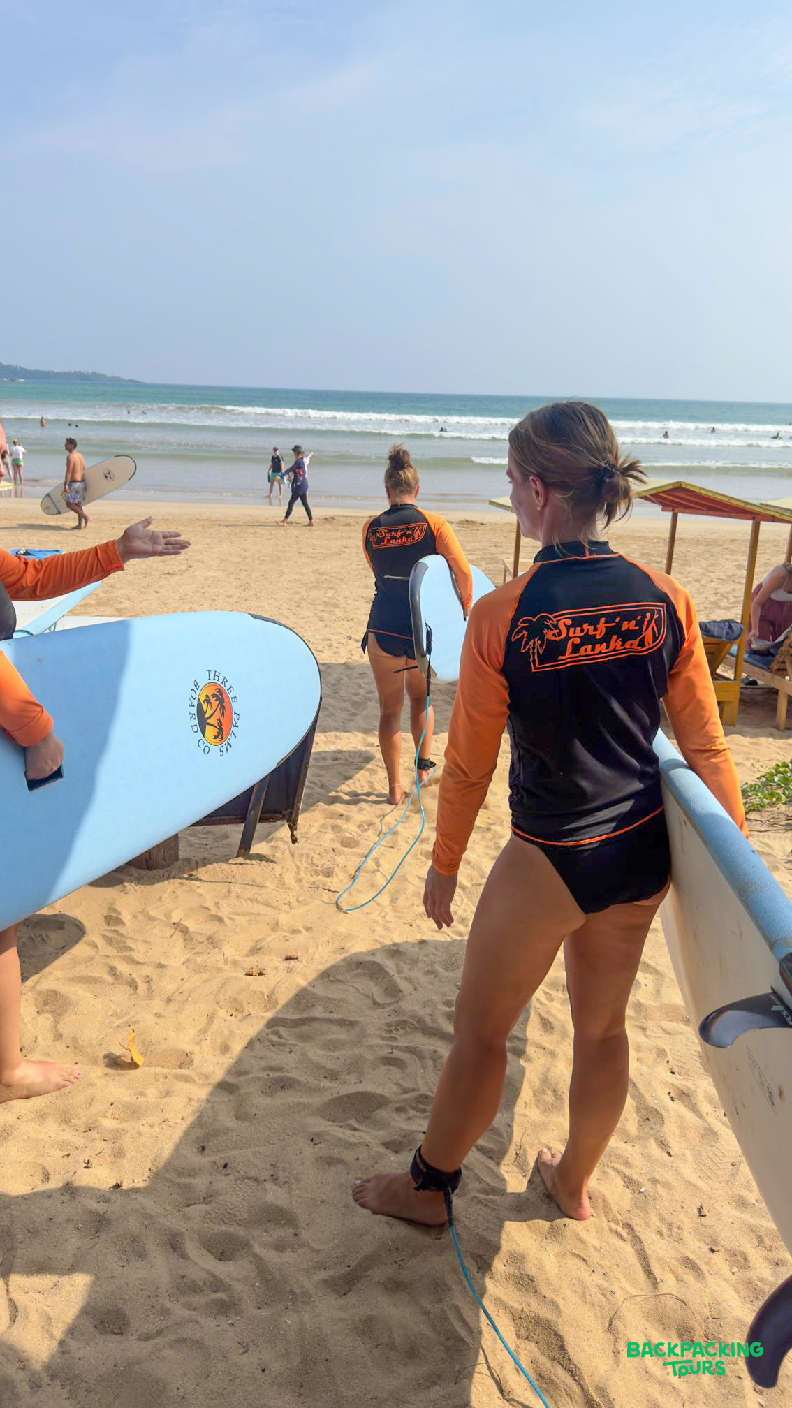 Women in rash guards holding surfboards on Weligama beach, heading towards the gentle waves.