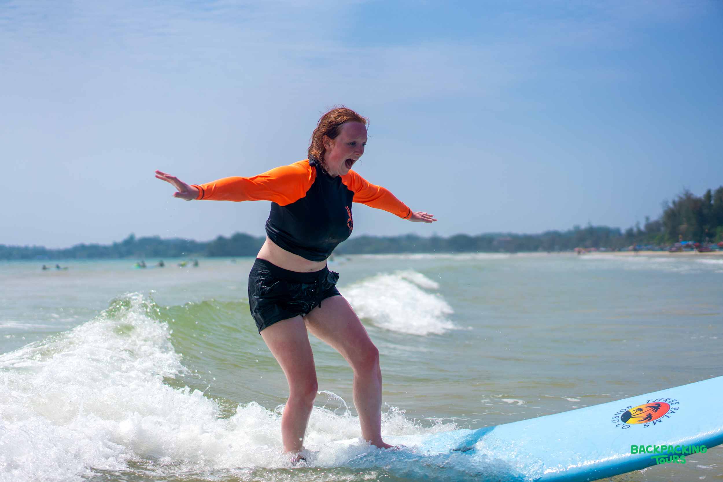 An excited woman learns to surf on a blue board at Weligama Beach, Sri Lanka.