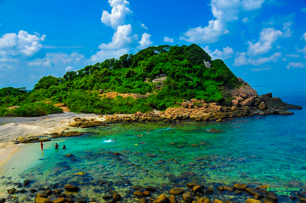 Swimmers enjoy the clear turquoise waters of Weligama beach in Sri Lanka with a lush island.