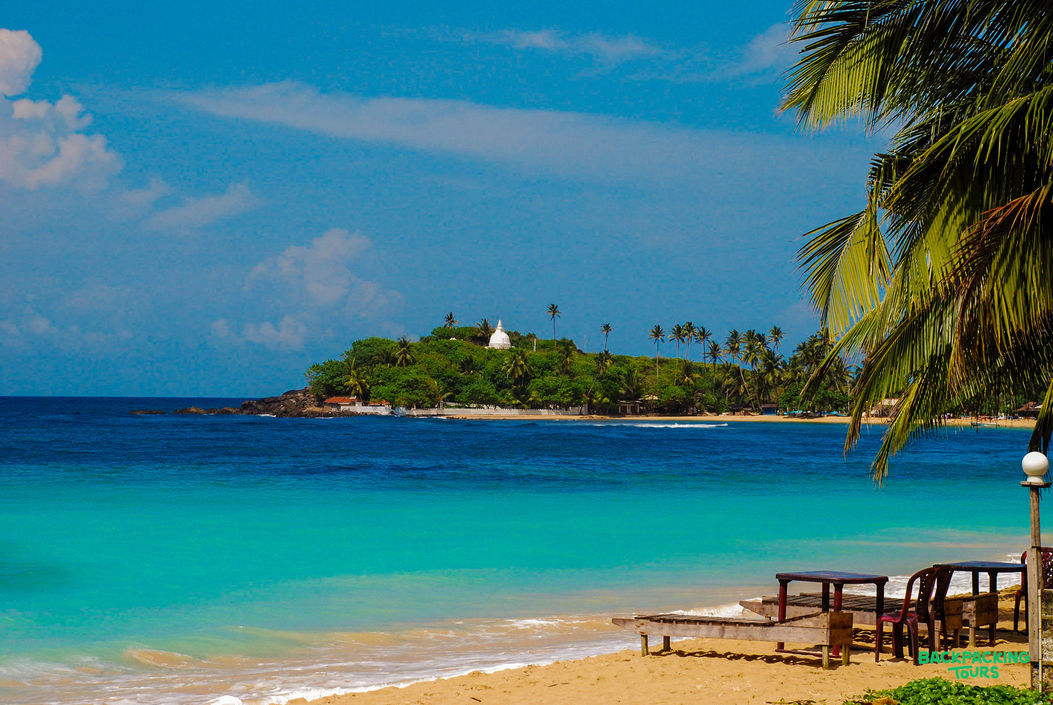 Tropical paradise at Weligama beach, Sri Lanka, with calm turquoise ocean and a palm-covered island.