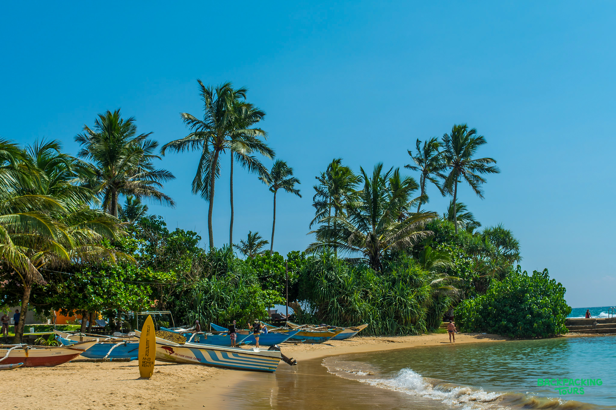 Sunny Mirissa beach with traditional fishing boats, lush palm trees, and calm turquoise water.