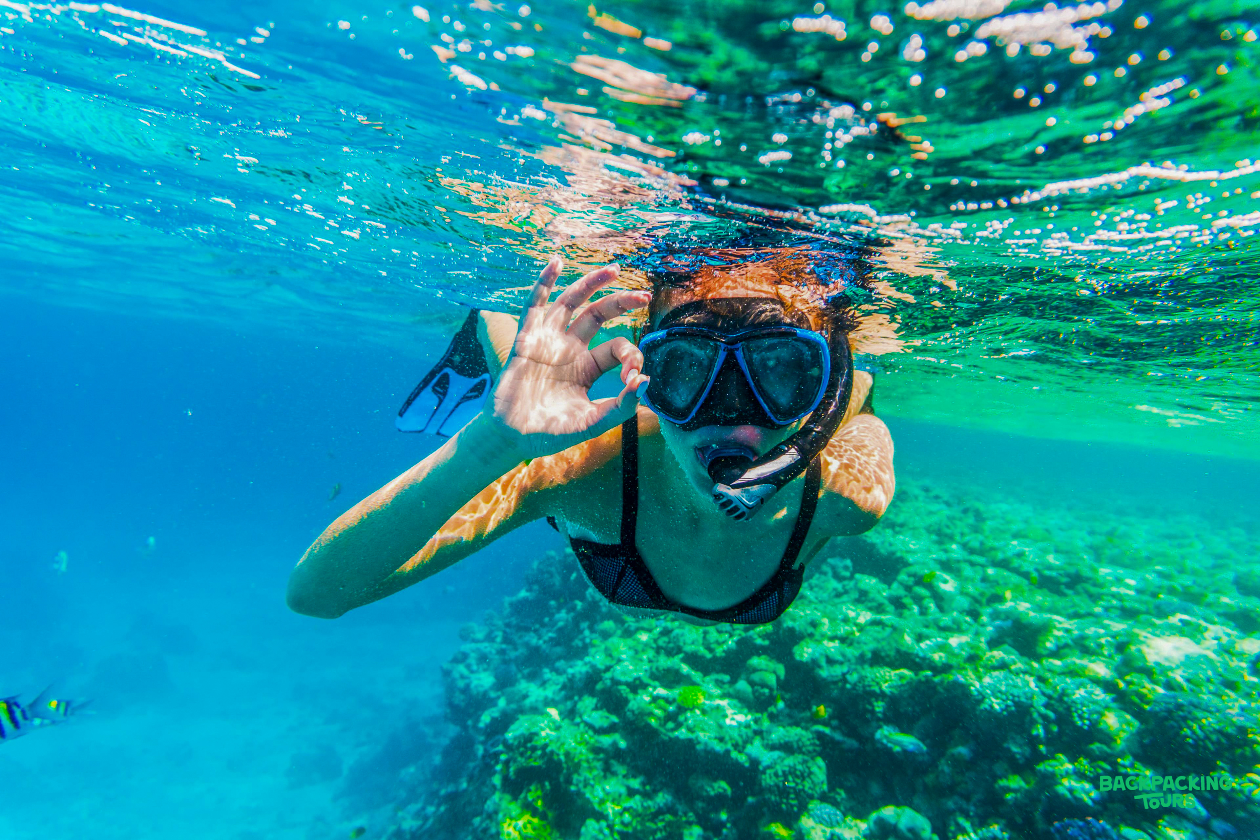 A woman enjoys snorkeling in the clear blue waters of Sri Lanka, giving an 'OK' sign.