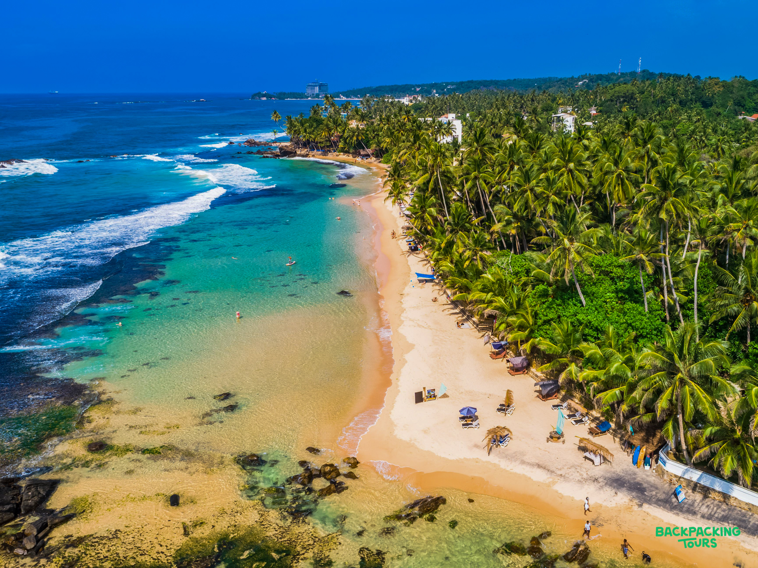 Stunning Weligama Beach, Sri Lanka, with clear turquoise water, golden sand, and lush palm trees.