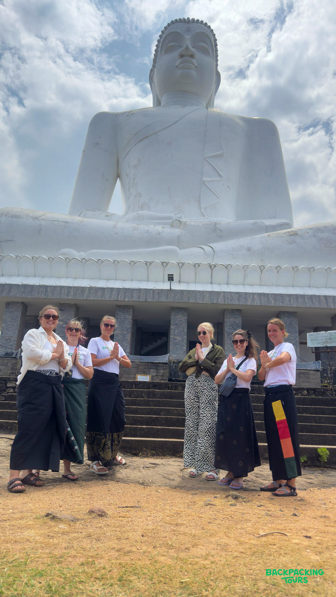 Six women stand in prayer pose before the enormous white Buddha statue in Dambulla.