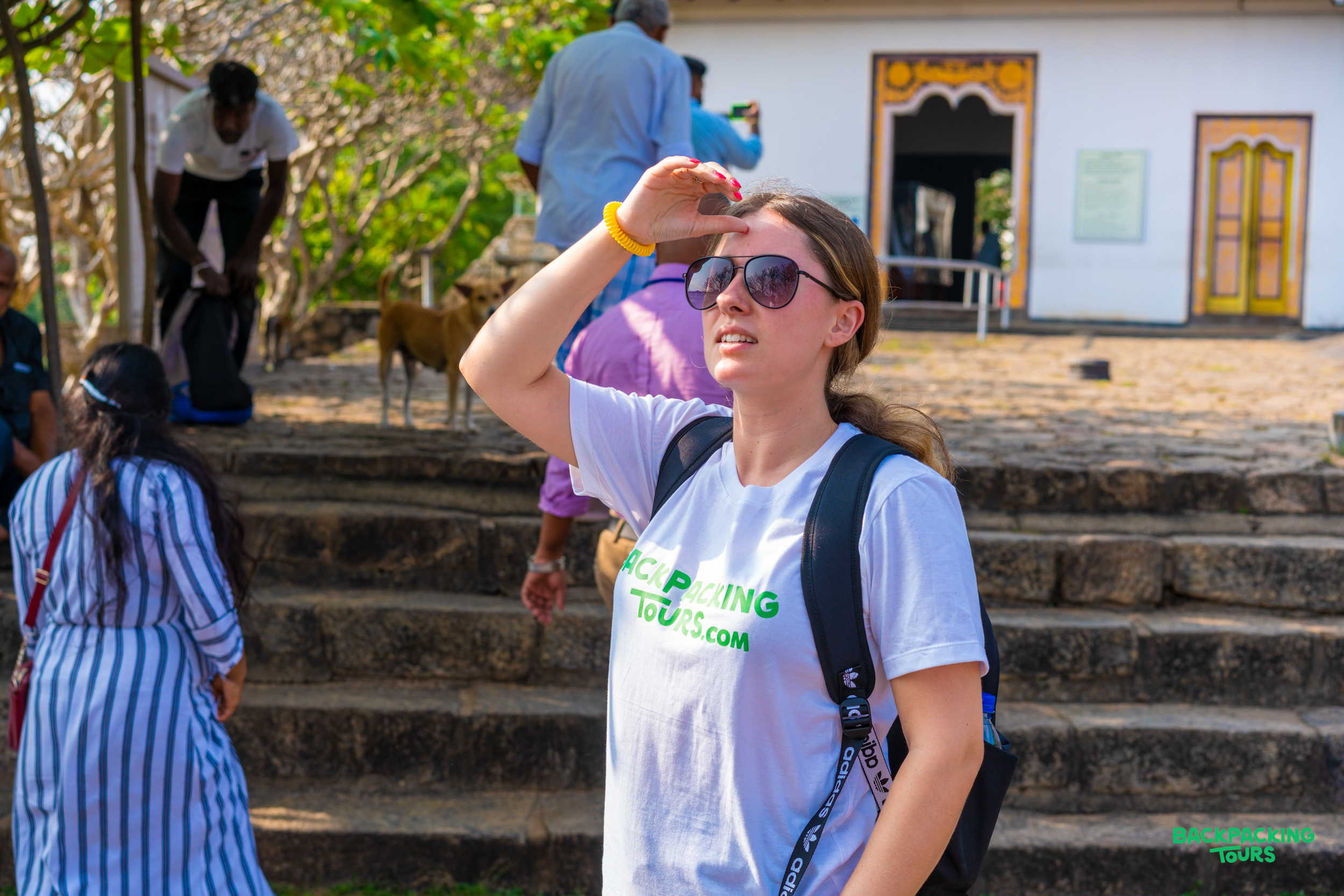 A young woman wearing sunglasses shields her eyes from the sun at the Dambulla Cave Temple.