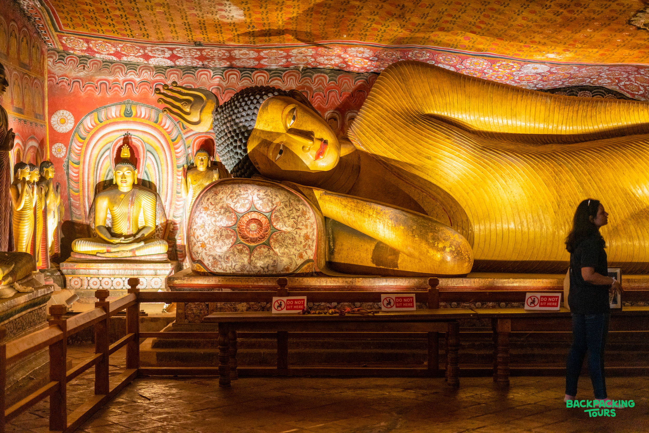 A traveler stands before the massive golden reclining Buddha statue in the Dambulla Cave Temple.