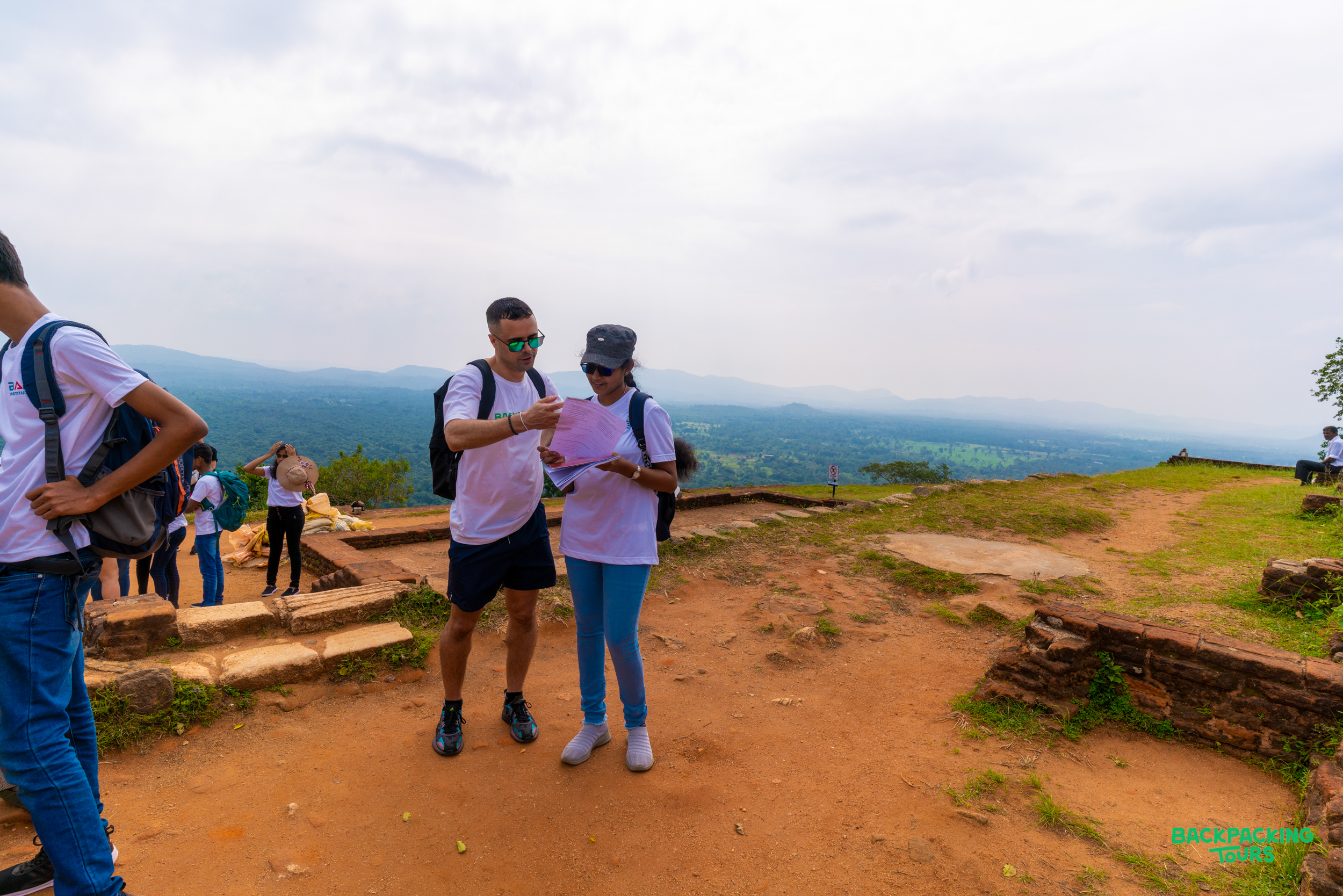 Two backpackers consult a map on top of Sigiriya Rock with a panoramic view.