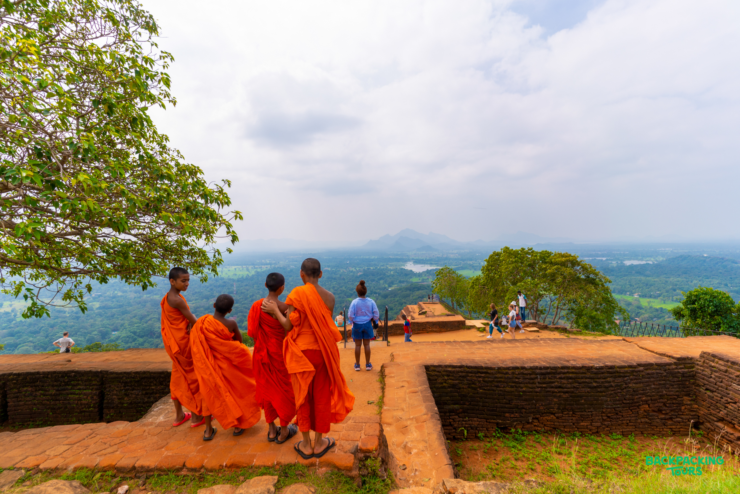 Four monks and a tourist admire the expansive green landscape from the ancient ruins of Sigiriya, Sri Lanka.