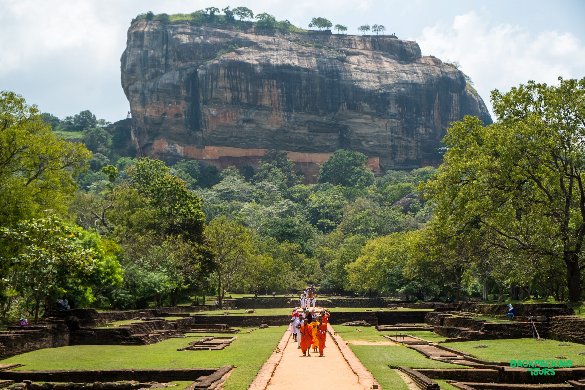 People walk through ancient water gardens towards the towering Sigiriya Lion Rock in Sri Lanka.