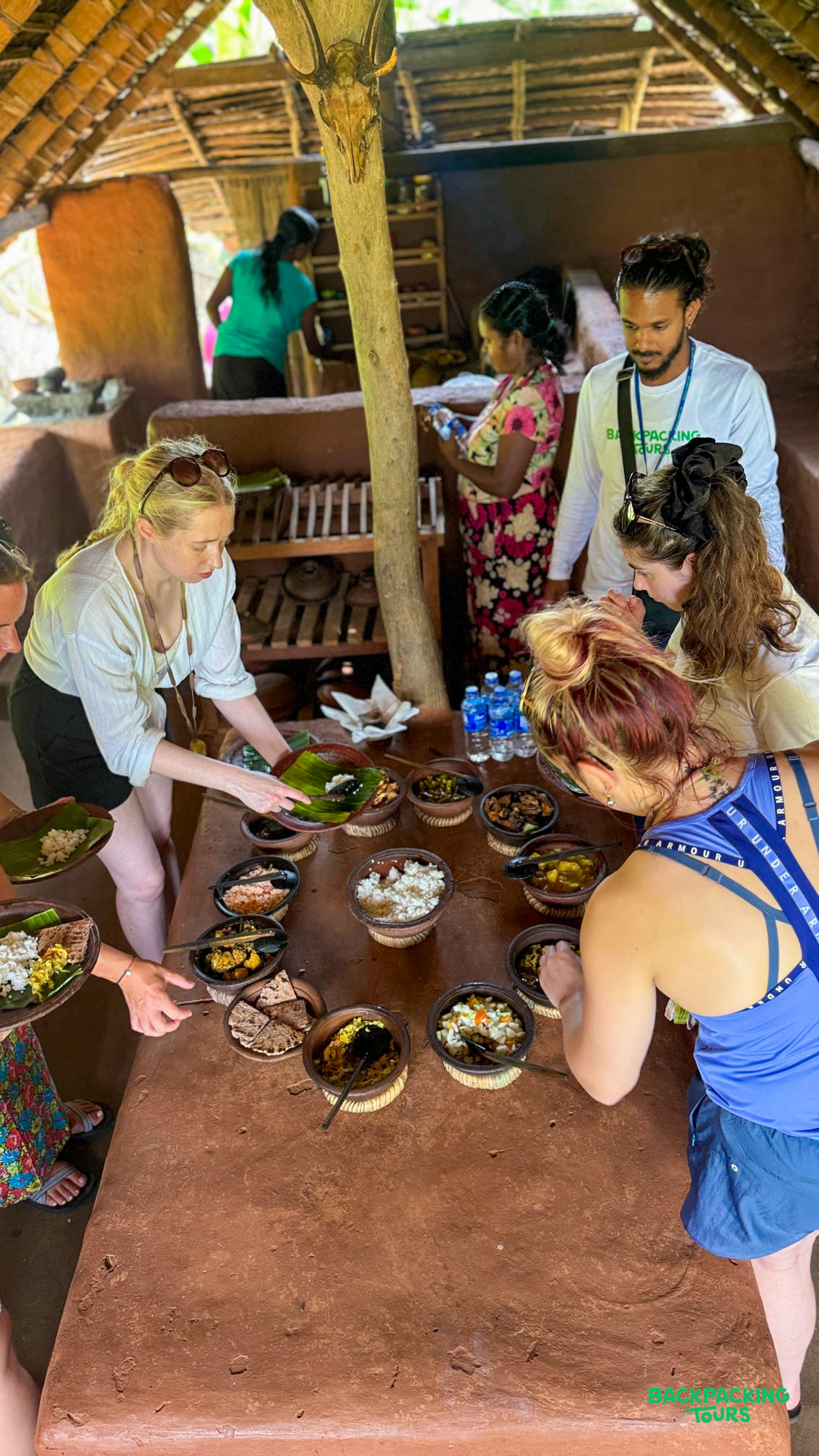 Backpackers serving themselves authentic Sri Lankan curry and rice from traditional clay pots in a Sigiriya village.