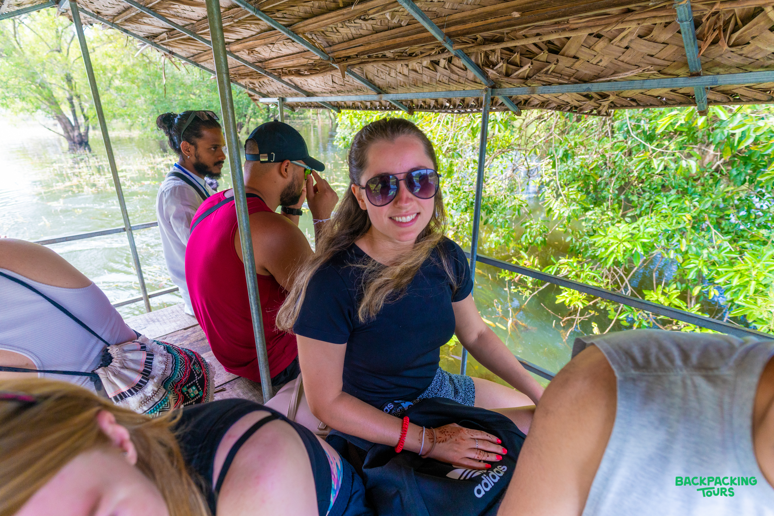 A smiling woman in sunglasses enjoys a boat ride through lush green waterways with fellow travelers.