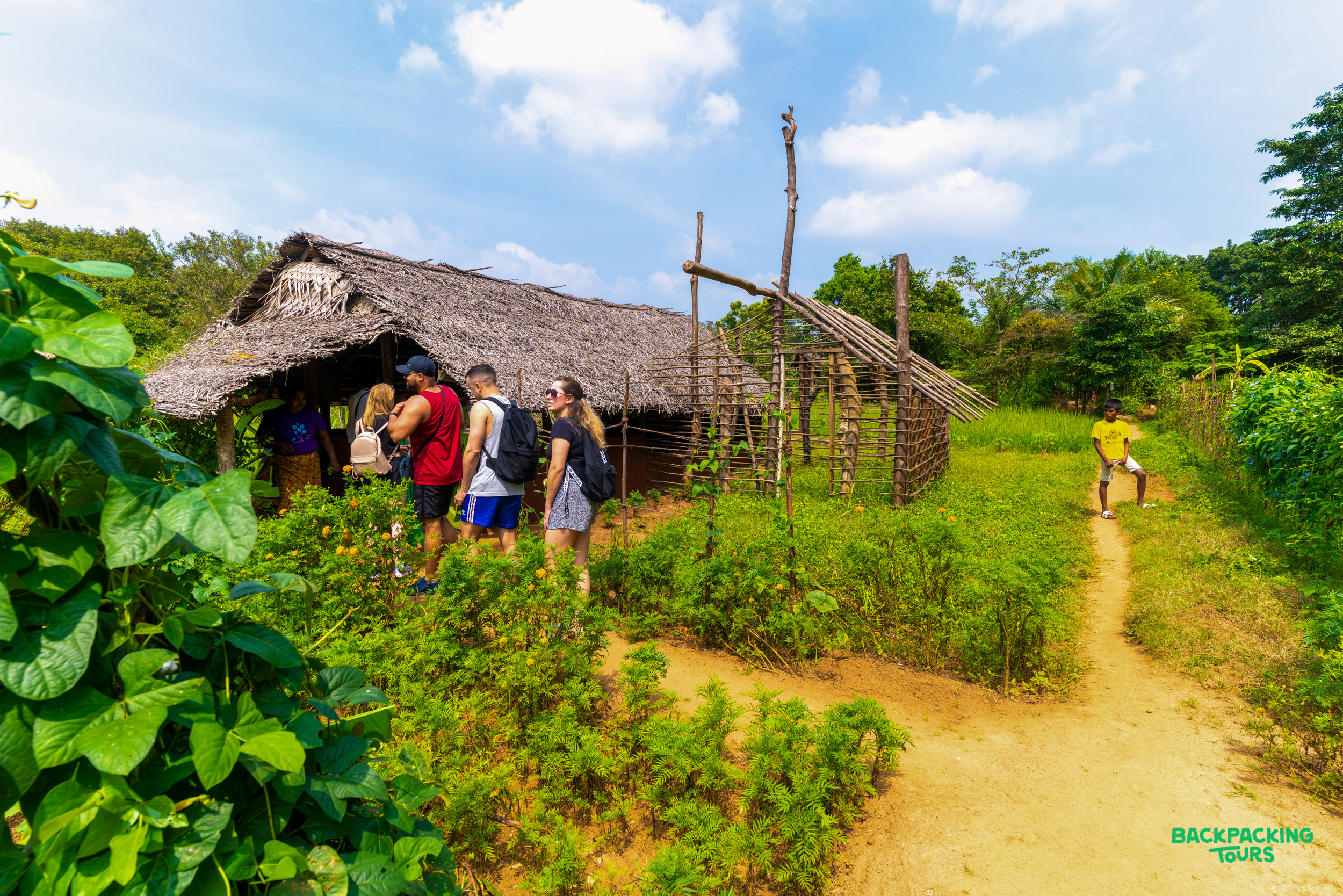 Backpackers explore a traditional village hut and lush surroundings on a cultural tour in Kandy.