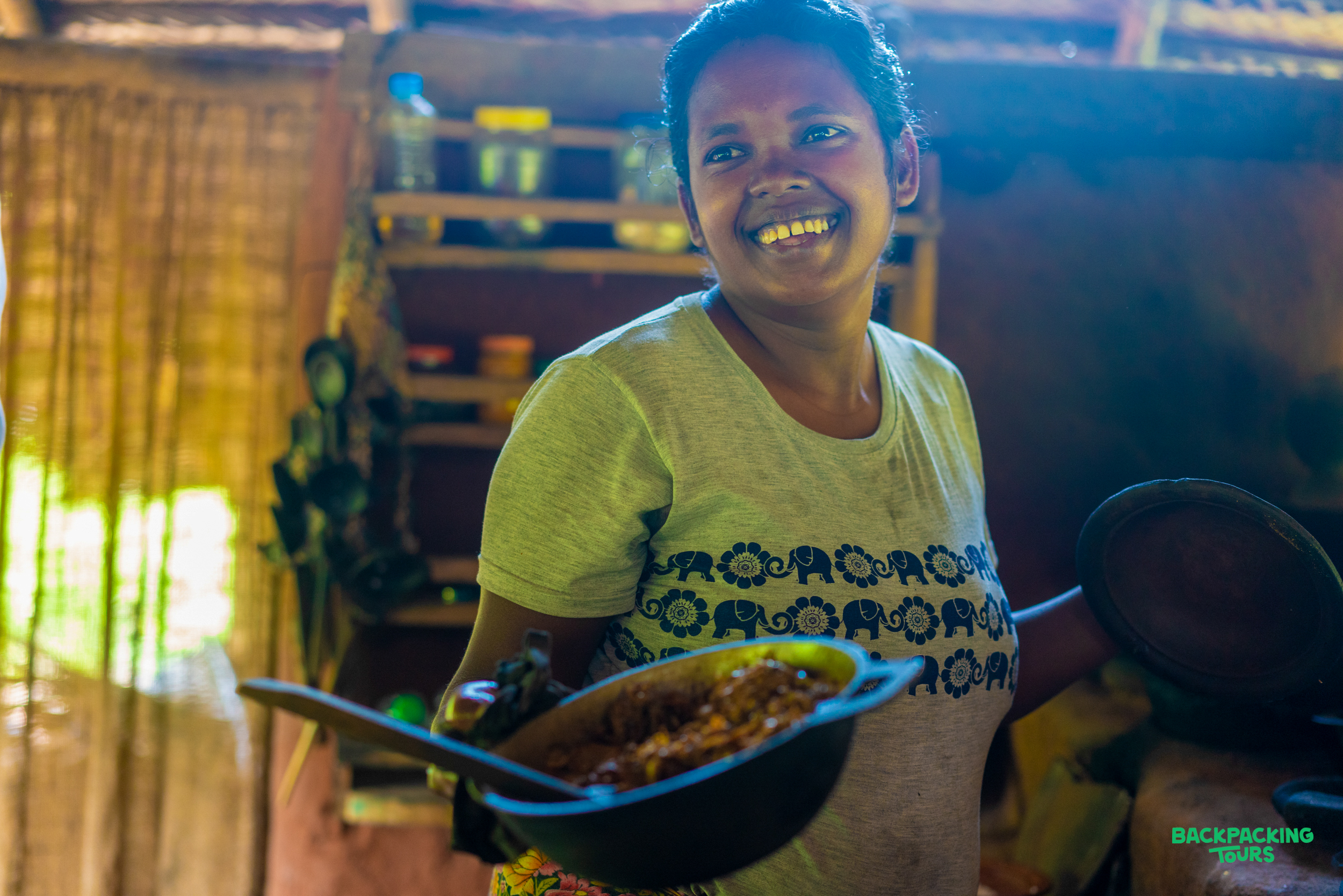 A smiling woman proudly presents a pot of traditional food during a village tour in Kandy.