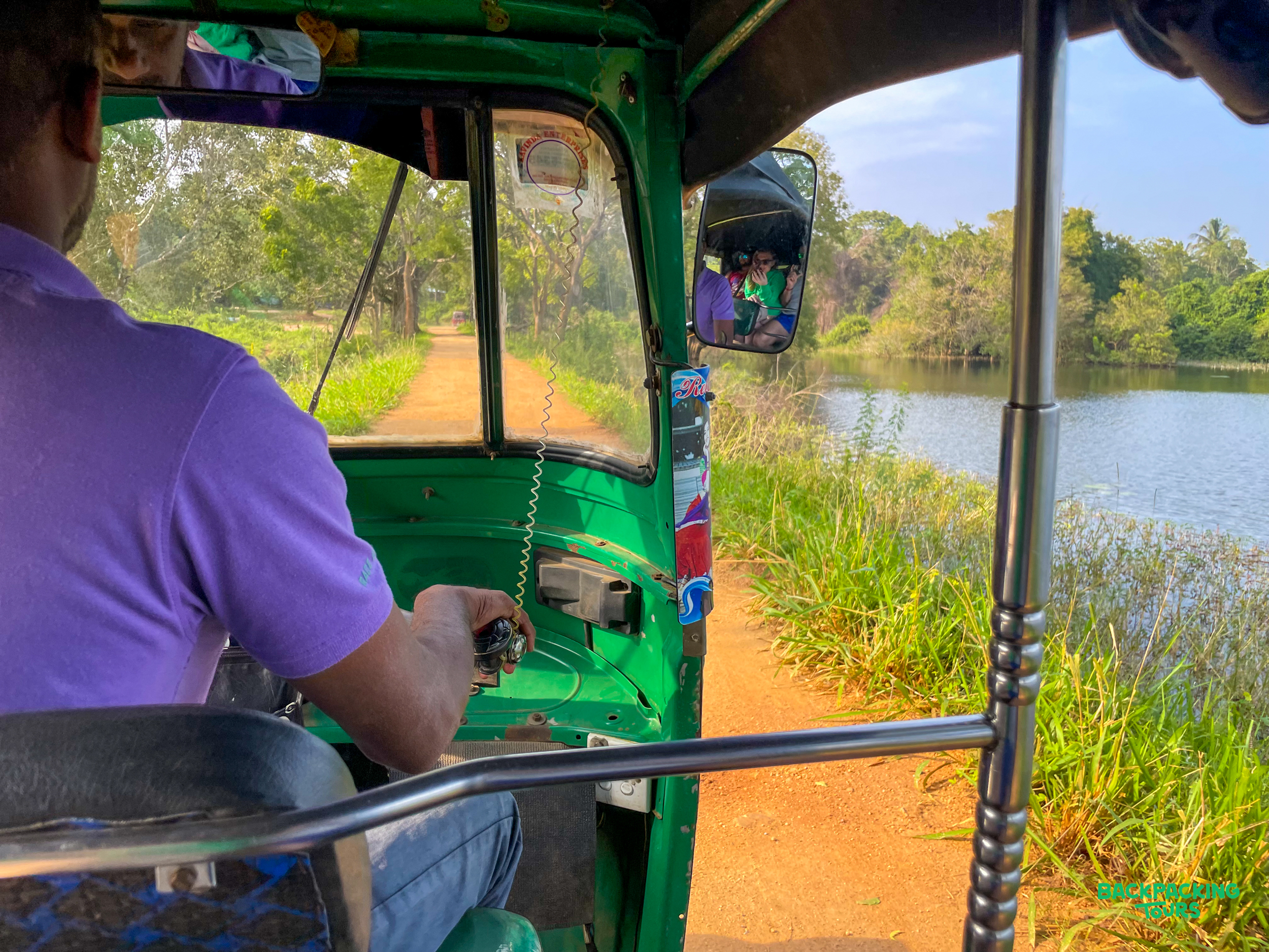 Enjoying a scenic tuk-tuk ride along a dirt road next to a lake in the Sri Lankan countryside.