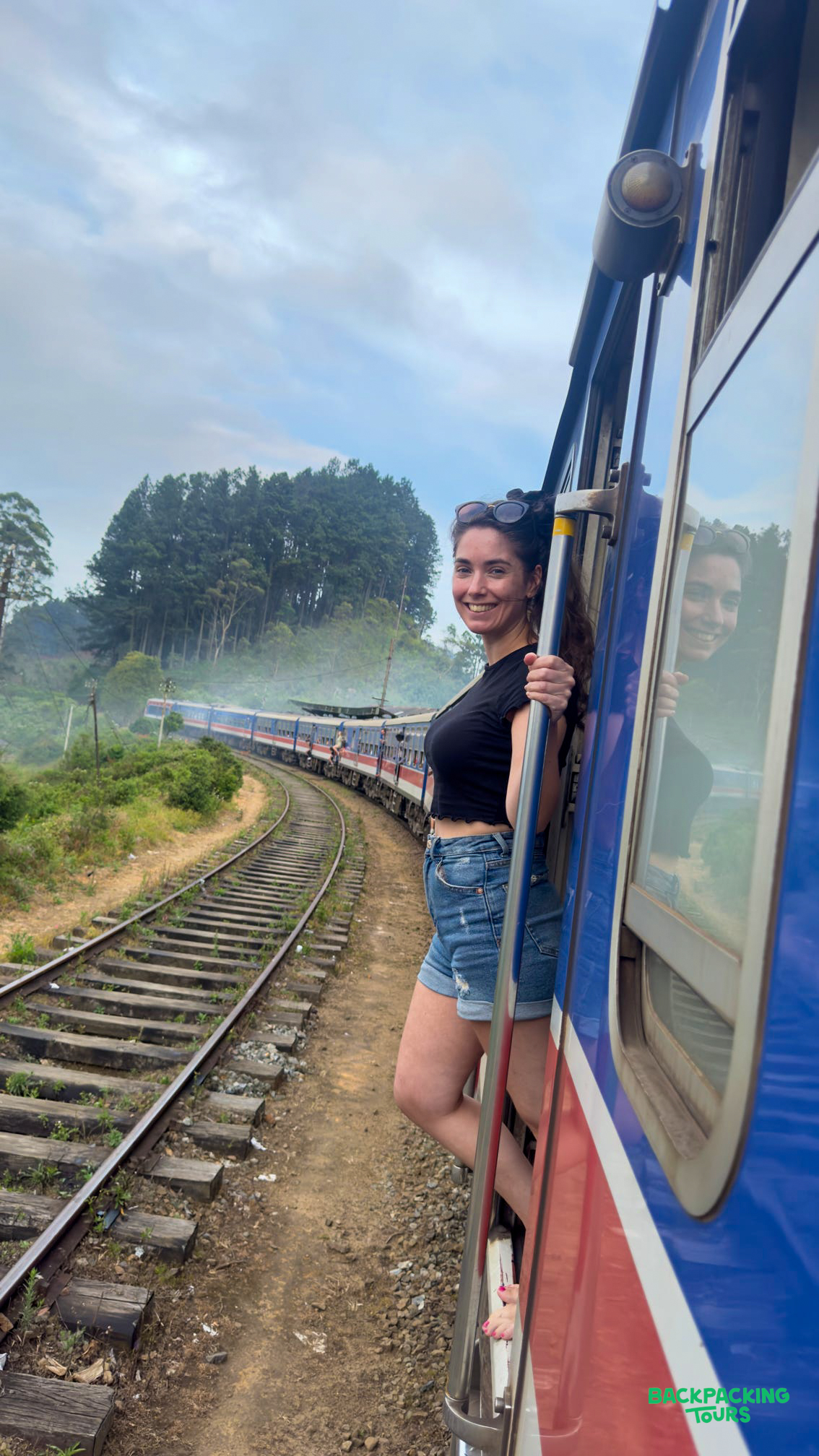 A smiling woman leans out of a blue train window, enjoying the scenic journey through Ella, Sri Lanka.