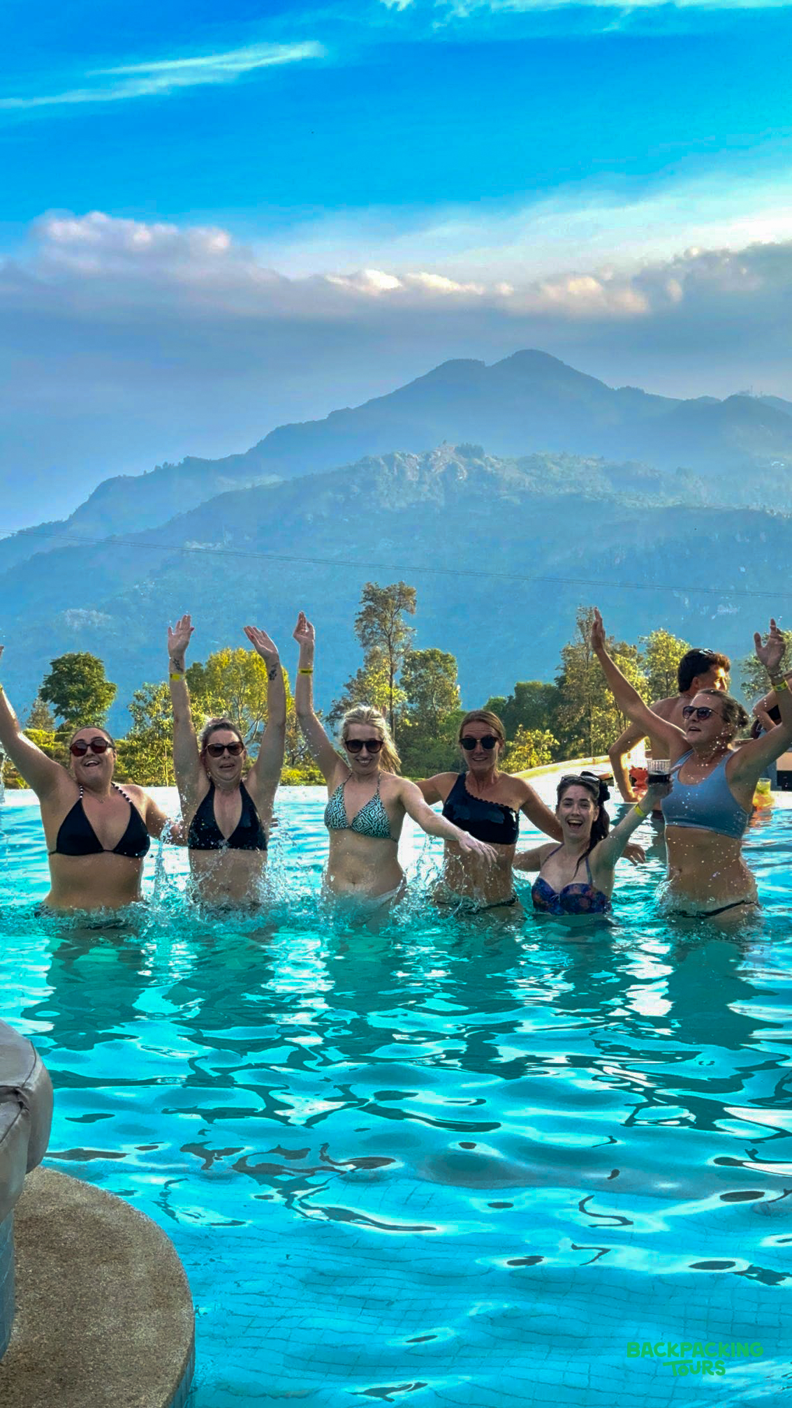 Six happy women splash in an infinity pool, enjoying the breathtaking mountain views of Ella.