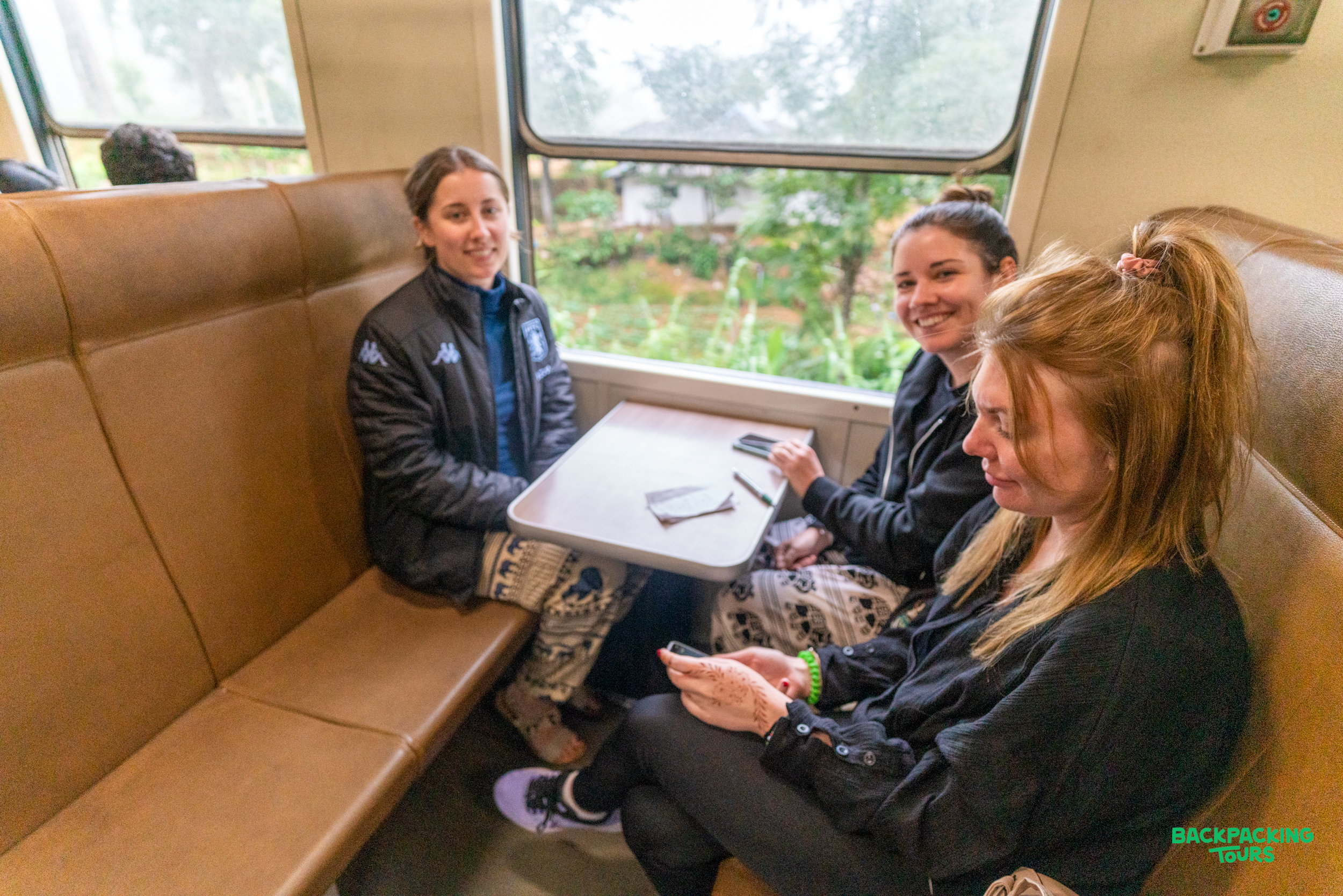 Three happy women enjoy a scenic train ride through the lush landscapes of Sri Lanka.