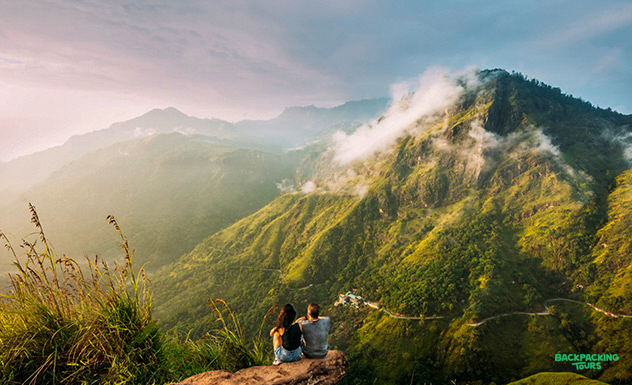 A couple sits on a mountain peak, admiring the breathtaking misty green landscapes of Ella, Sri Lanka.