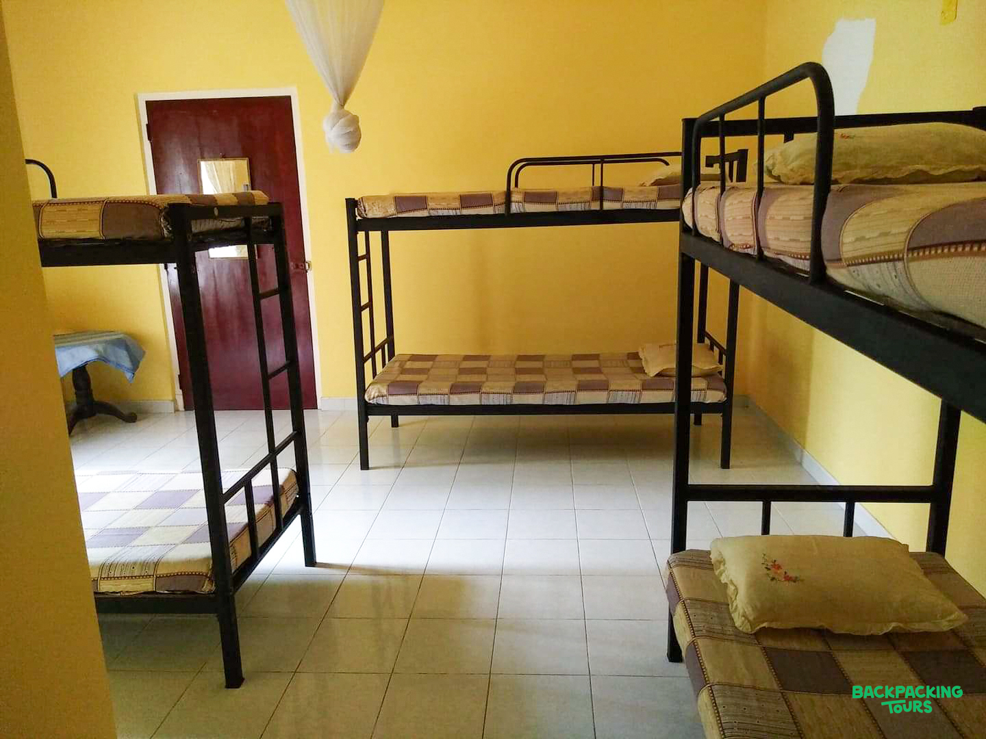 A bright yellow dormitory room with multiple bunk beds and tiled floors, ready for backpackers.