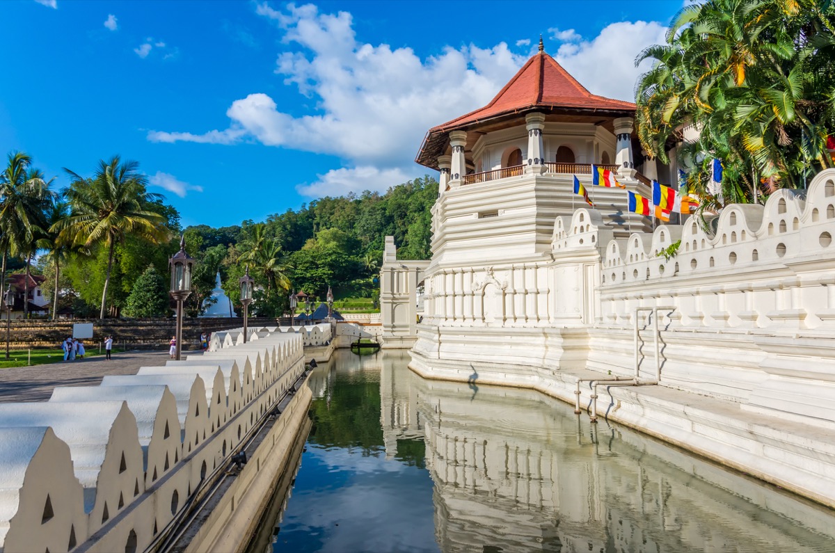 Stunning white temple with a red roof and colorful flags reflected in calm water in Sri Lanka.