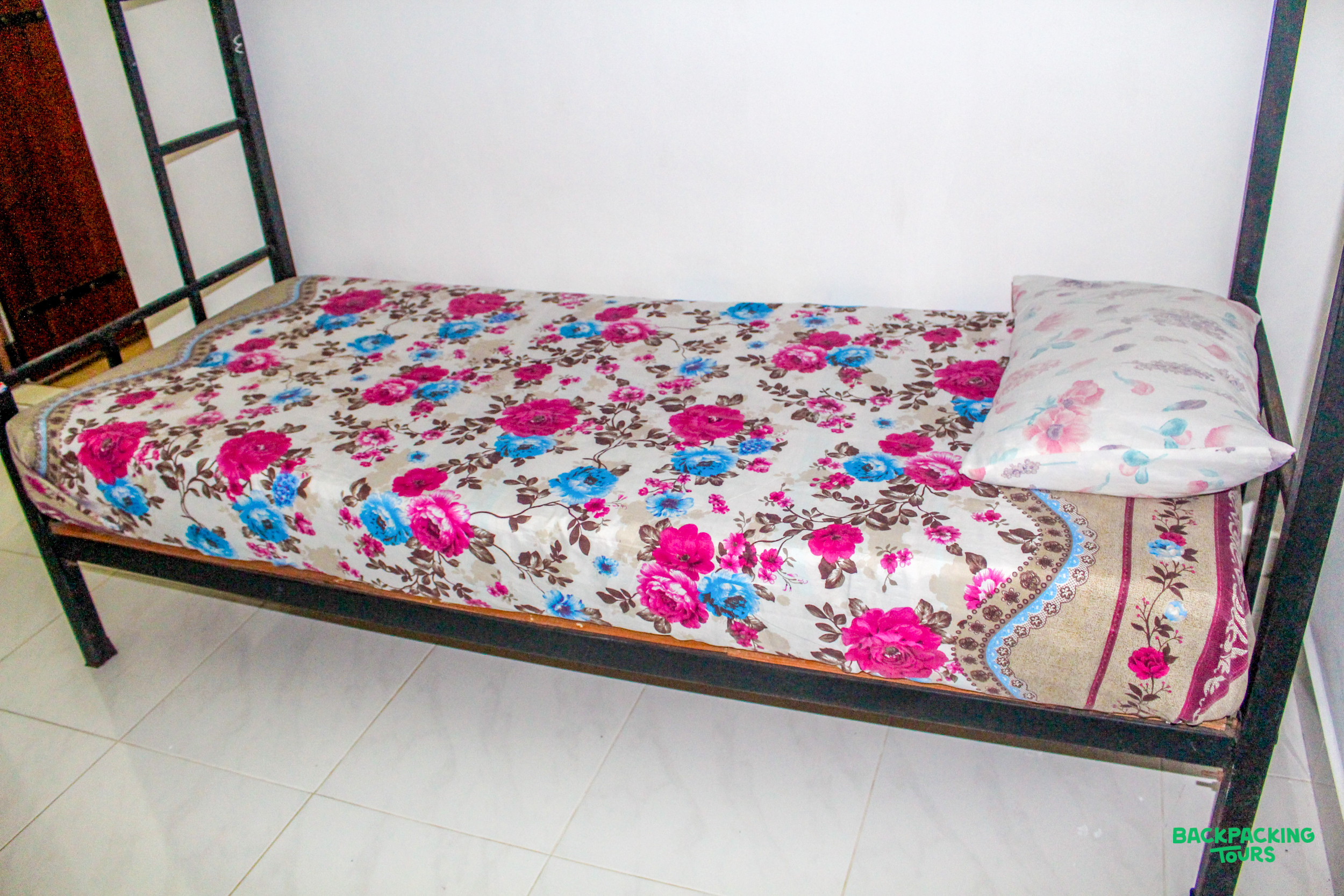 A comfortable single bed with a bright floral bedcover and pillow in simple accommodation.