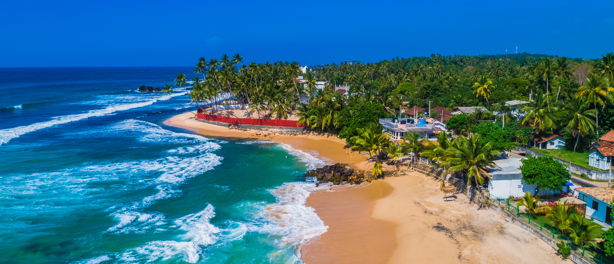 Beautiful tropical beach with turquoise ocean waves, golden sand, and lush palm trees in Sri Lanka.