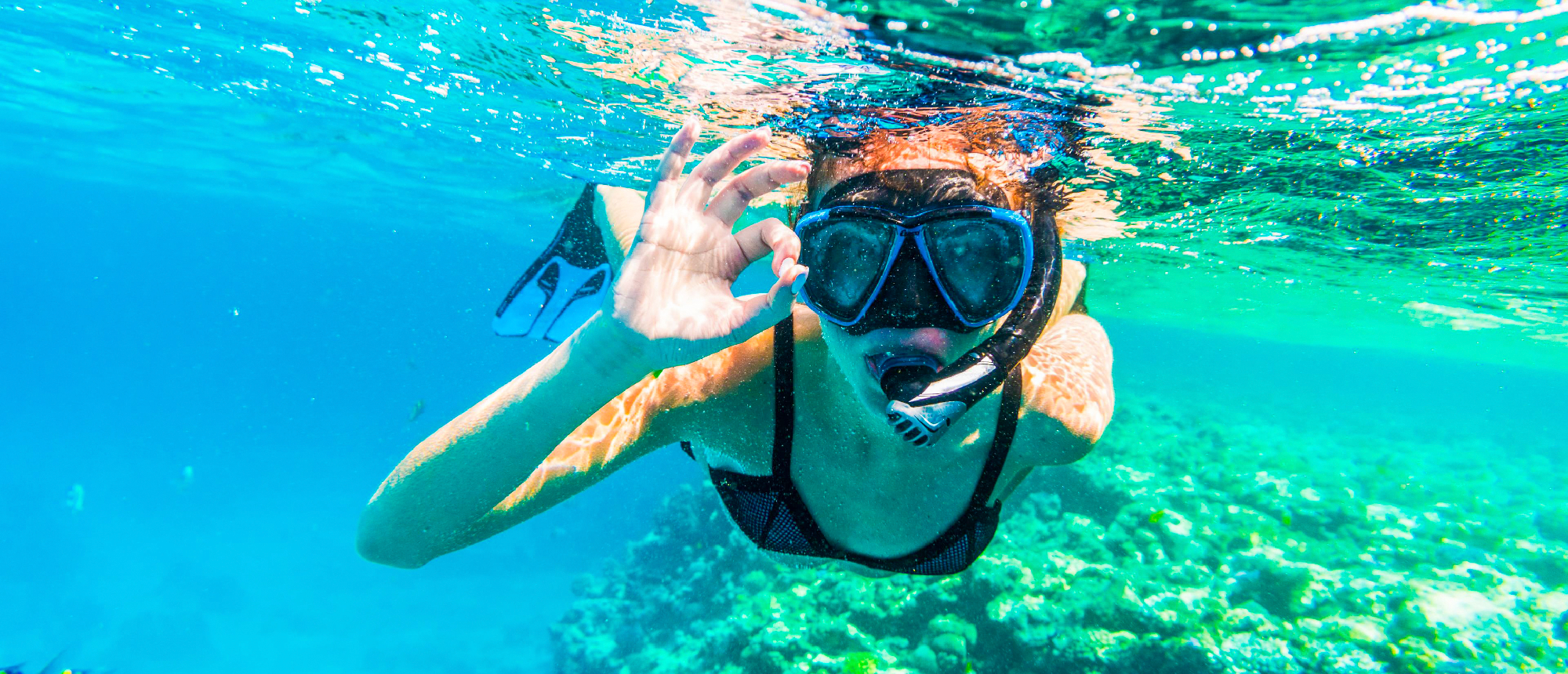 Happy woman snorkeling in clear blue water near Mirissa, Sri Lanka, giving an OK sign.
