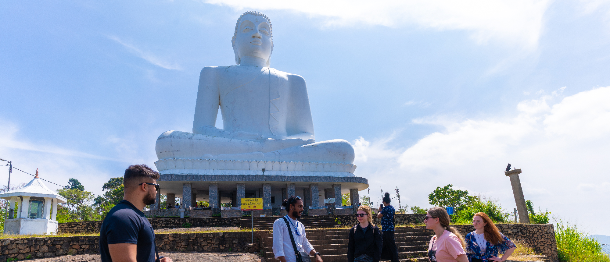 Tourists admire the giant white sitting Buddha statue under a clear sky in Dambulla, Sri Lanka.