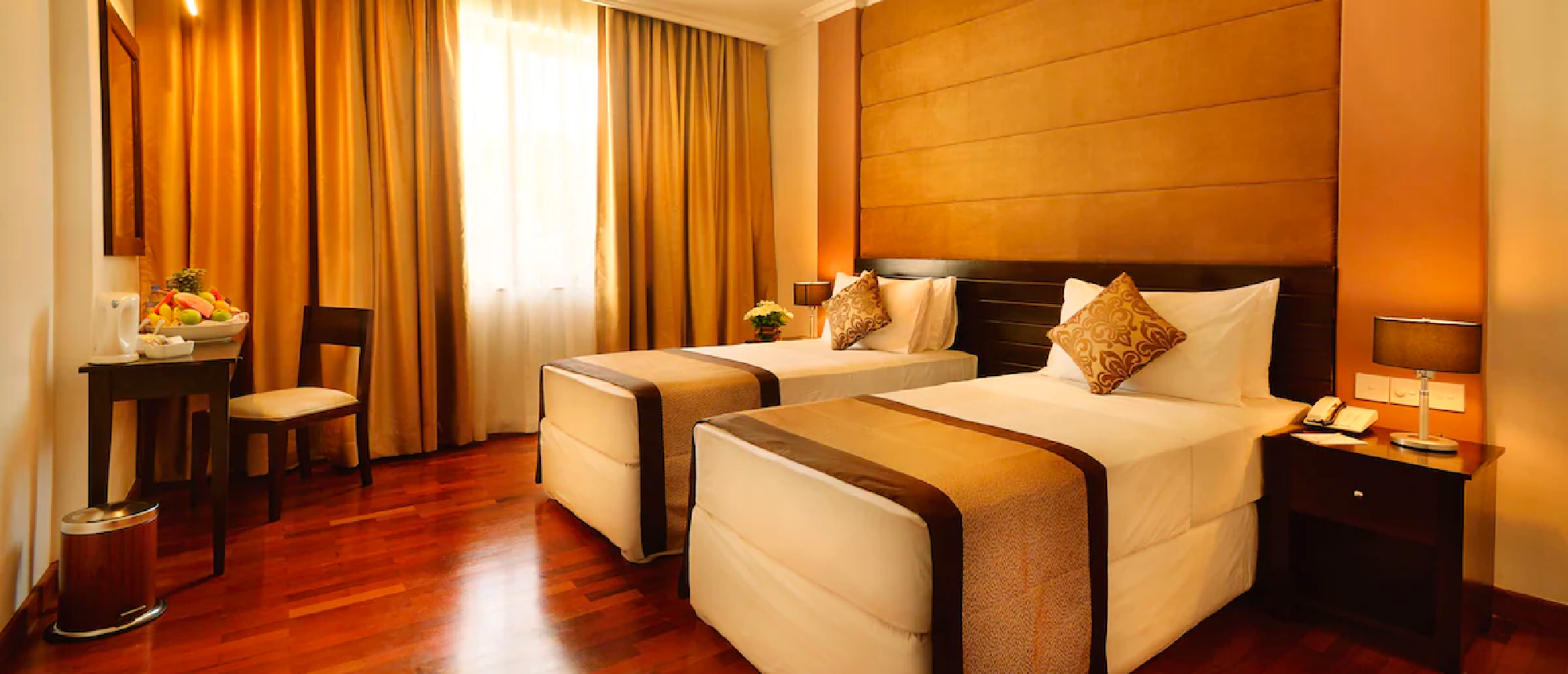 A comfortable hotel room with two single beds, wooden floors, and warm orange decor.